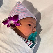 Rose joined the competition — help win amazing prizes! baby, infant, child, sleeping, pacifier, knit_hat, striped_clothing, swaddled, blanket, bed, flower, purple_flower, portrait, sunlight, shadow, indoors, peaceful, face, newborn, cozy