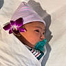 baby, infant, child, sleeping, pacifier, knit_hat, striped_clothing, swaddled, blanket, bed, flower, purple_flower, portrait, sunlight, shadow, indoors, peaceful, face, newborn, cozy