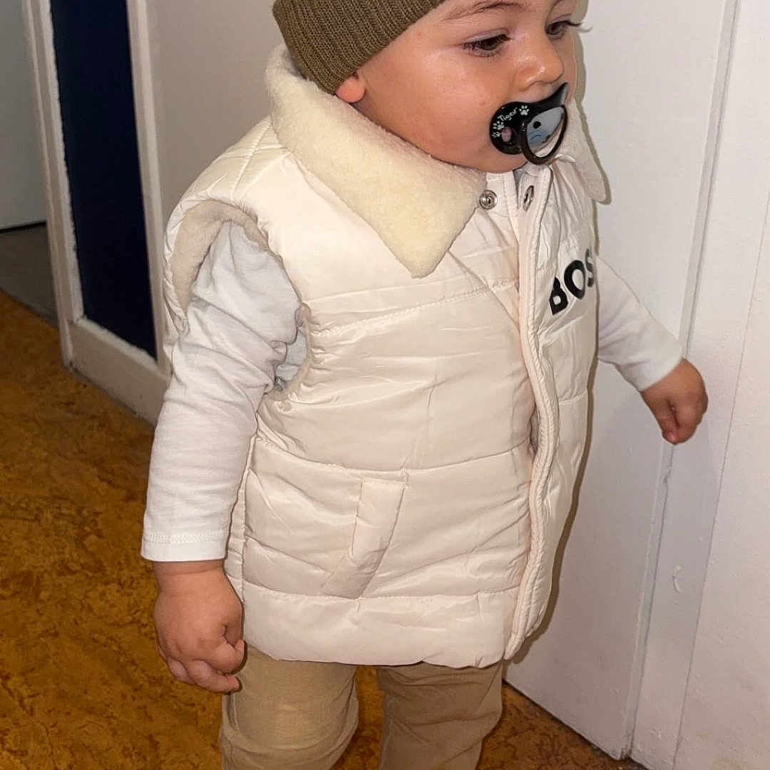 Nelyo Guillotot participe au concours pour gagner de l'argent avec cette photo : baby, beanie, brown_pants, casual, child, cute, door, floor, indoor, pacifier, person, portrait, side_view, socks, standing, toddler, vest, warm_clothing, white_clothing, young_child