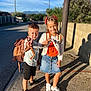 Nino participe au concours pour gagner de l'argent avec cette photo : children, boy, girl, backpack, peace_sign, sidewalk, sunlight, smiling, casual_clothing, braided_hair, shorts, skirt, sneakers, outdoor, daytime, shadow, street, happy, posing, blue_sky