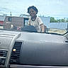 child, smiling, car_dashboard, car_interior, hood, outdoor, van, building, sky, cloudy, person, casual_clothing, dreadlocks, urban, parking_lot, vehicle, young, happy, daylight, relaxed