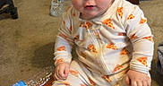 John is registered to the contest to win money with this photo: baby, child, onesie, pizza_pattern, shower_cap, spongebob, carpet, plastic_bottle, toy, indoor, cute, sitting, face, foot, hand, curious, clothing, person, floor, home