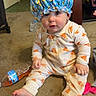 baby, child, onesie, pizza_pattern, shower_cap, spongebob, carpet, plastic_bottle, toy, indoor, cute, sitting, face, foot, hand, curious, clothing, person, floor, home