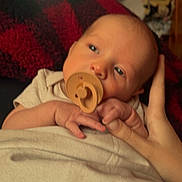Daxsyn is registered to the contest to win money with this photo: baby, pacifier, hand, blanket, wooden_wall, infant, closeup, soft_lighting, indoor, skin, person, sleepy, cozy, warm_tones, newborn, portrait, resting, candid, comfort, holding_hand