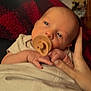 baby, pacifier, hand, blanket, wooden_wall, infant, closeup, soft_lighting, indoor, skin, person, sleepy, cozy, warm_tones, newborn, portrait, resting, candid, comfort, holding_hand