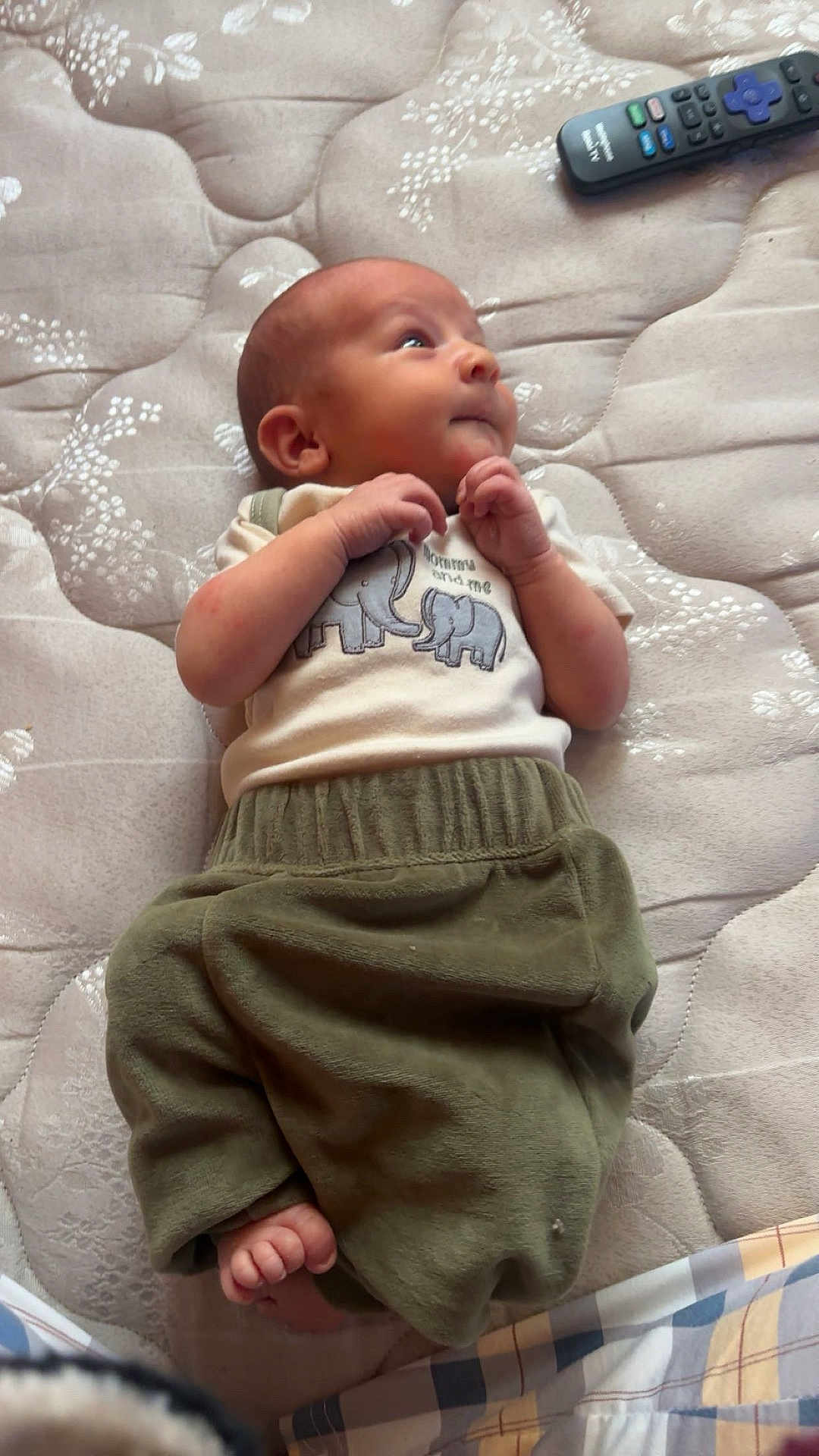Daxsyn is registered to the contest to win money with this photo: baby, infant, mattress, clothing, elephant_design, green_pants, remote_control, foot, hand, face, person, laying_down, curious, indoor, soft_texture, pattern, sleepwear, child, newborn, cute