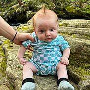 Hayden is registered to the contest to win money with this photo: baby, clothing, face, grass, head, hosiery, land, nature, outdoors, pants, person, photography, plant, portrait, rock, shorts, sitting, sock, tree, vegetation