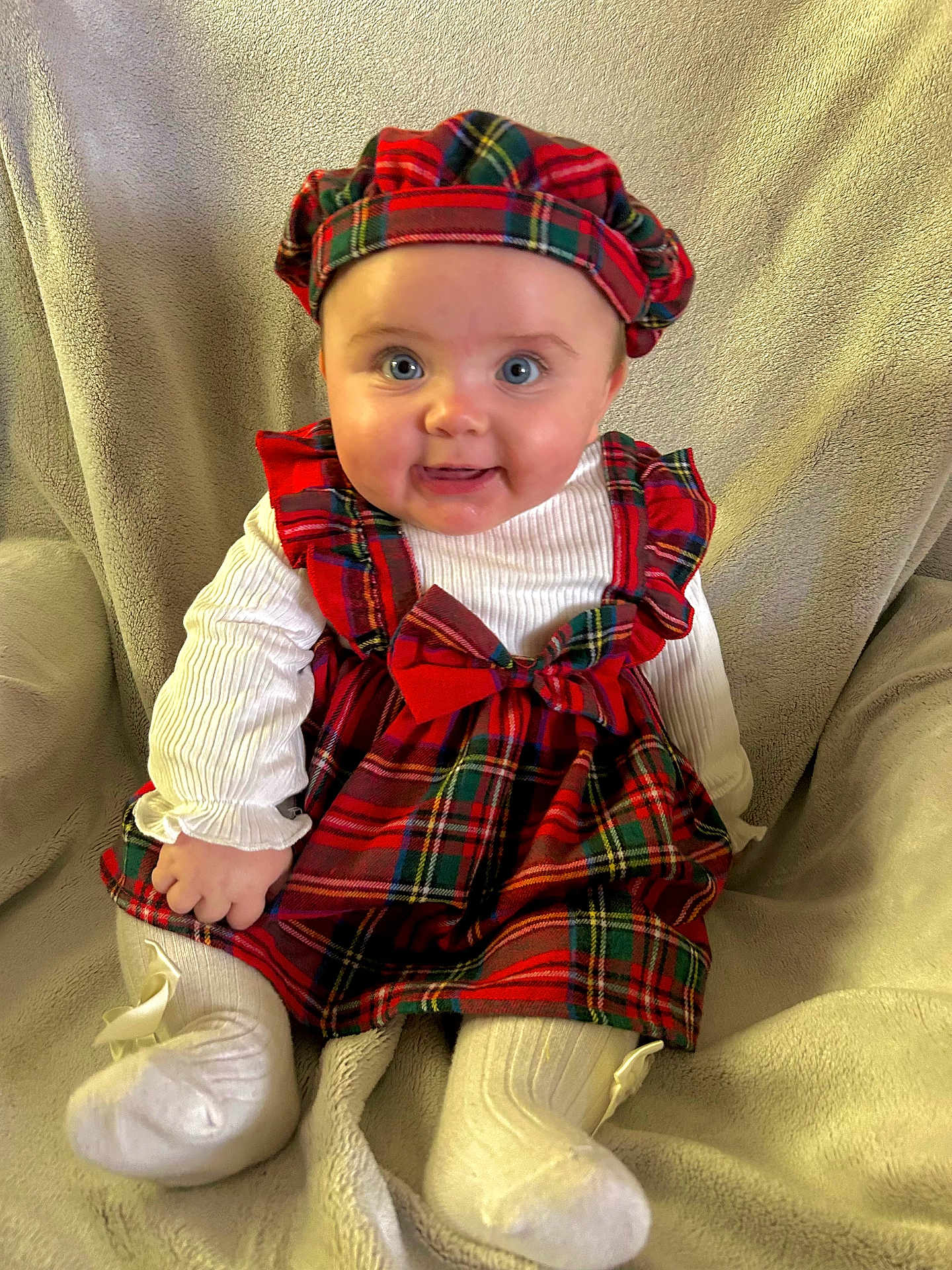 Emma a rejoint le concours — aidez-le/la à gagner de superbes lots ! baby, child, plaid_dress, hat, white_tights, smiling, blue_eyes, sitting, blanket, indoors, cute, portrait, festive, soft_texture, happy, young_child, fashion, cozy, infant, clothing