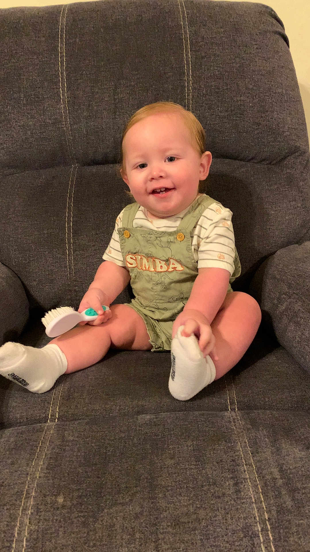Adelio joined the competition — help win amazing prizes! toddler, child, smiling, indoor, chair, cushion, clothing, socks, hairbrush, person, cute, happy, seated, baby, overalls, green, white, skin, face, legs