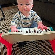 Dean is registered to the contest to win money with this photo: baby, child, toy_piano, striped_shirt, blue_eyes, carpet, indoor, furniture, couch, floor, hands, playing, curious, portrait, person, young_child, striped_clothing, wooden_toy, flooring, expression