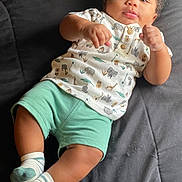 Quadarius is registered to the contest to win money with this photo: baby, infant, child, clothing, shirt, shorts, socks, animal_print, curly_hair, skin, face, eyes, hands, legs, footwear, bed, quilt, relaxing, indoors, portrait