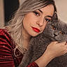 woman, cat, portrait, close_up, indoor, red_lipstick, gray_cat, amber_eyes, silver_hair, hugging, cozy, calm, intimate, face, pet, feline, cute, warm, soft_texture, casual_clothing