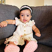 Kiaana is registered to the contest to win money with this photo: baby, infant, dress, headband, pink_shoes, couch, sofa, smile, big_eyes, bracelet, arm, buttons, sitting, indoors, living_room, fabric, portrait, cute, child, footwear