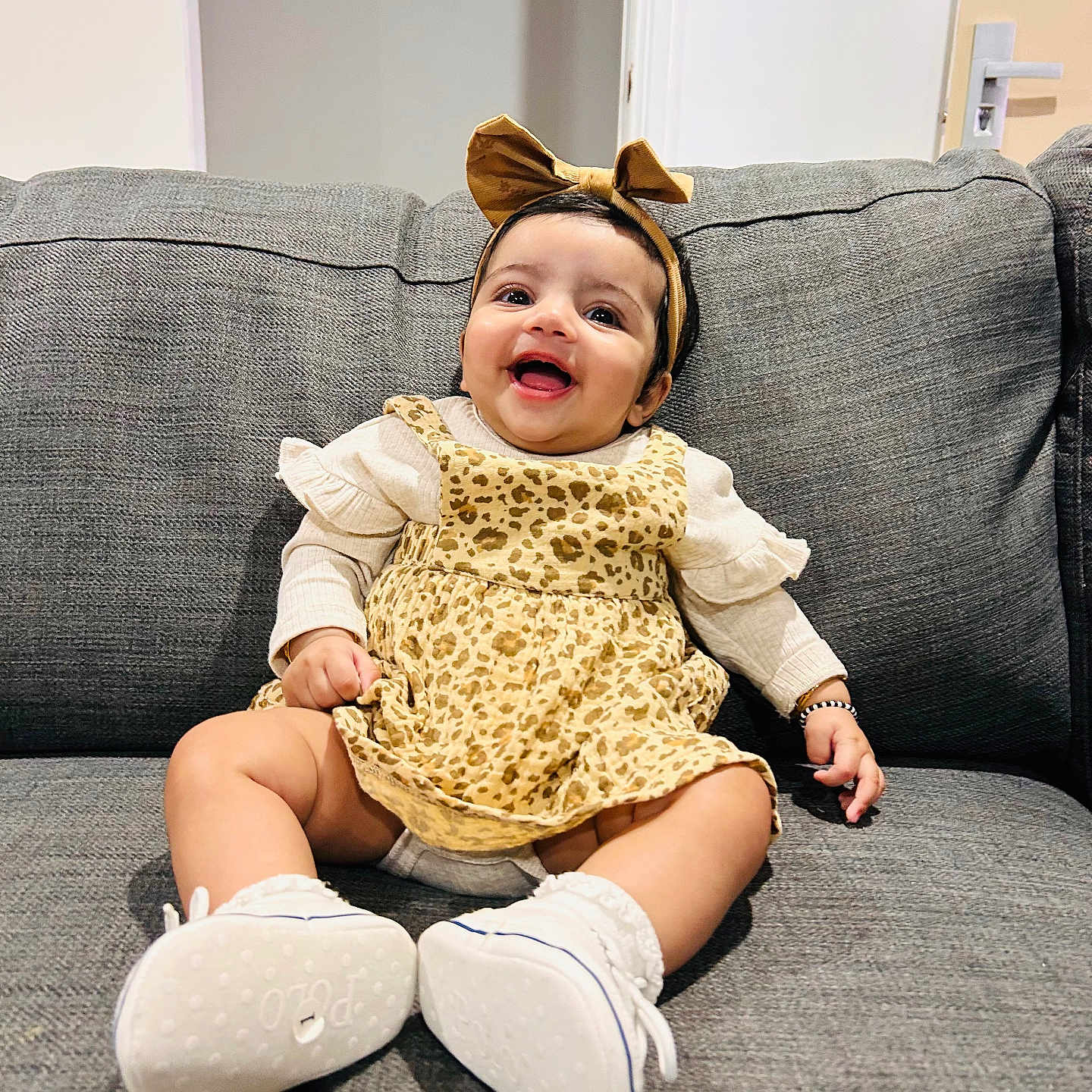 Kiaana joined the competition — help win amazing prizes! baby, bow, couch, door, dress, eyes, furniture, hands, happy, headband, infant, leopard_print, living_room, portrait, sitting, smile, socks, sofa, wall, white_shoes
