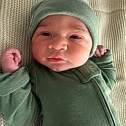 Gray is registered to the contest to win money with this photo: baby, infant, child, green_clothing, hat, blanket, lying_down, fist, face, headwear, newborn, portrait, cute, soft_texture, cozy, sleepwear, young_child, indoors, person, closeup