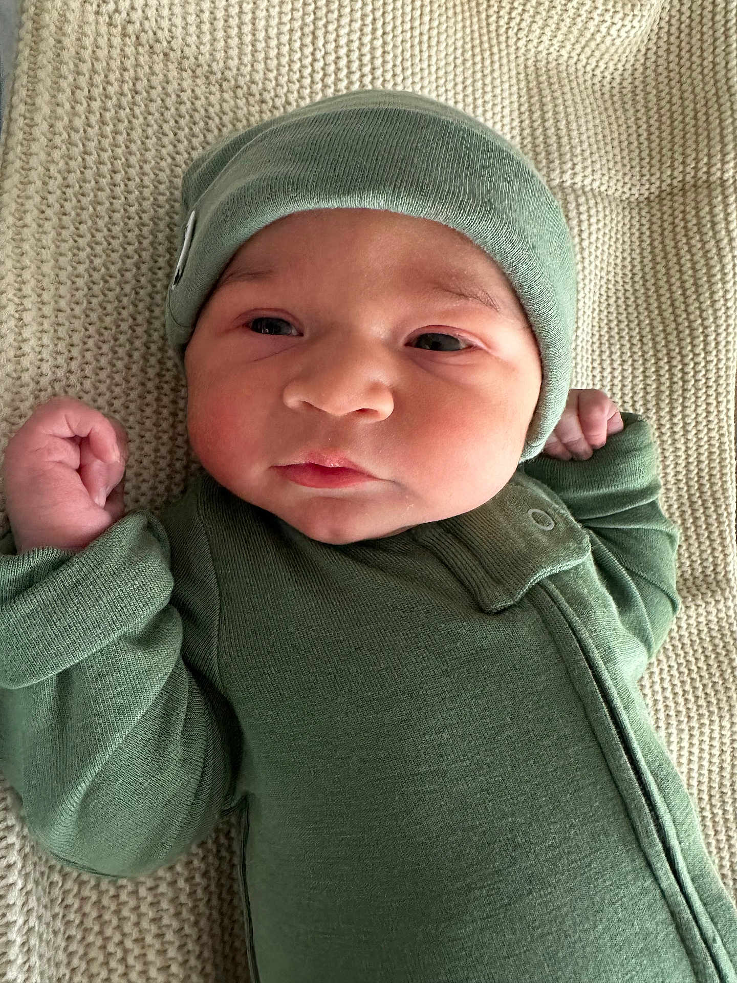 Gray is registered to the contest to win money with this photo: baby, infant, child, green_clothing, hat, blanket, lying_down, fist, face, headwear, newborn, portrait, cute, soft_texture, cozy, sleepwear, young_child, indoors, person, closeup