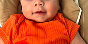Estebàn participe au concours pour gagner de l'argent avec cette photo : baby, child, infant, orange_shirt, ribbed_clothing, cushion, beige, face, eyes, smile, skin, head, person, portrait, closeup, comfortable, cute, young, lying_down, indoor
