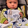 baby, child, blanket, car_seat, dinosaur_pattern, green_clothing, indoor, infant, portrait, cute, young_child, seated, hands, face, eyes, expression, soft_texture, cozy, comfort, warm