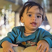 Vihaan a rejoint le concours — aidez-le/la à gagner de superbes lots ! child, toddler, face, hands, sweater, cushion, indoor, portrait, curly_hair, expression, young, person, casual_clothing, soft_lighting, blurred_background, warm_colors, cute, looking_at_camera, close_up, cozy