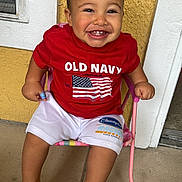 Joseph joined the competition — help win amazing prizes! baby, barefoot, casual_clothing, child, concrete_floor, cute, face, happy, indoor, old_navy, person, pink_chair, portrait, red_shirt, shorts, sitting, smiling, toddler, white_trim, yellow_wall