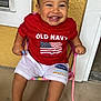 baby, barefoot, casual_clothing, child, concrete_floor, cute, face, happy, indoor, old_navy, person, pink_chair, portrait, red_shirt, shorts, sitting, smiling, toddler, white_trim, yellow_wall
