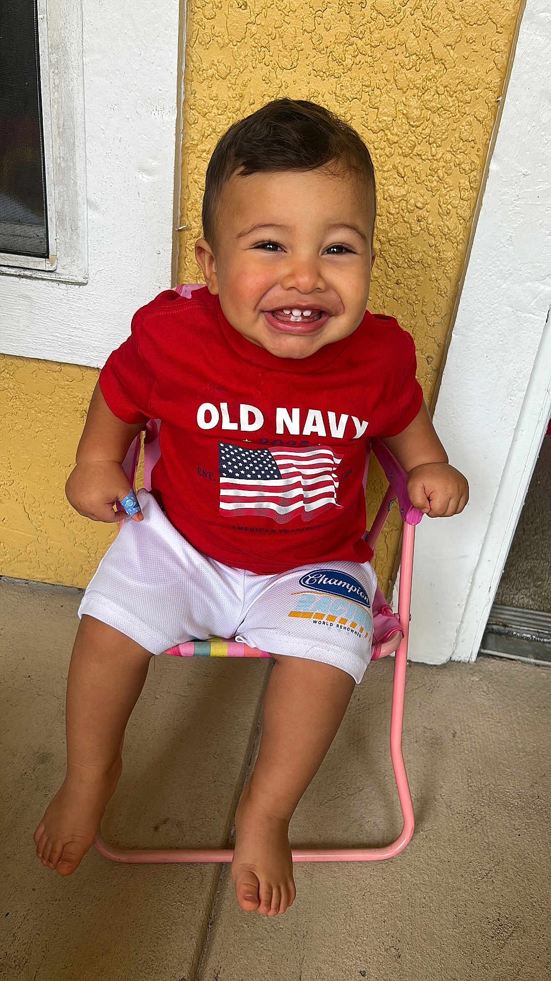 Joseph joined the competition — help win amazing prizes! baby, barefoot, casual_clothing, child, concrete_floor, cute, face, happy, indoor, old_navy, person, pink_chair, portrait, red_shirt, shorts, sitting, smiling, toddler, white_trim, yellow_wall