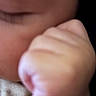 Brayden is registered to the contest to win money with this photo: baby, infant, child, close_up, face, cheek, mouth, hand, fist, skin, portrait, blurry, soft_focus, indoor, dark_background, clothing, fabric, cuddling, human, photograph