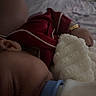 baby, infant, sleeping, red_outfit, white_teddy_bear, stuffed_animal, pacifier, blanket, bed, bedroom, cozy, dim_lighting, closeup, baby_clothing, wristband, plush_toy, cuddling, resting, indoor, portrait