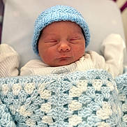 Luca is registered to the contest to win money with this photo: newborn, baby, sleeping, blanket, crocheted_blanket, blue_hat, knit_hat, bassinet, hospital, infant, cozy, cute, peaceful, soft, warm, clothing, person, portrait, resting, child