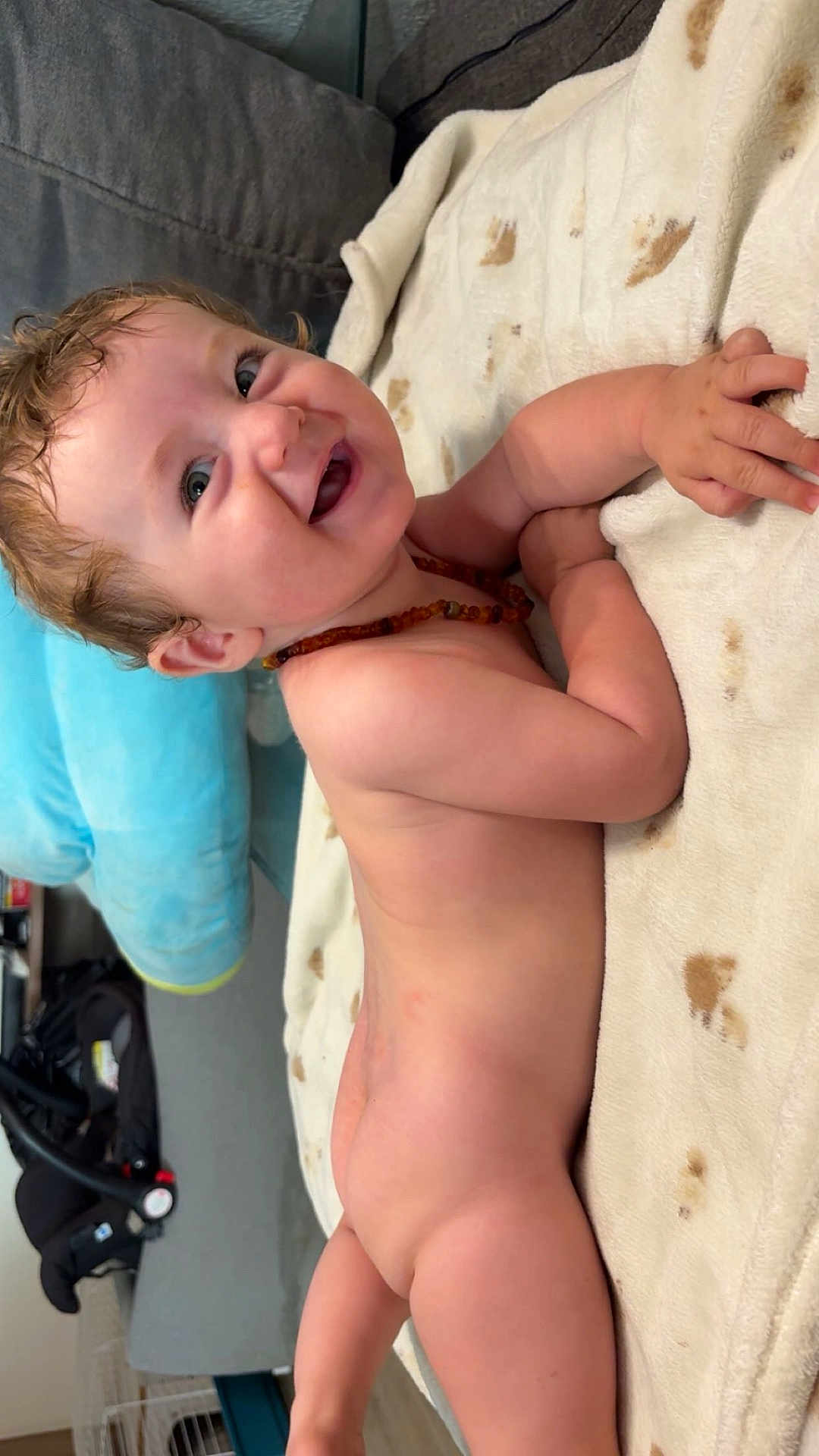 Aaron a rejoint le concours — aidez-le/la à gagner de superbes lots ! baby, smiling, curly_hair, blanket, naked, indoor, couch, car_seat, happy, infant, child, skin, face, head, hand, person, home, floor, toy, necklace