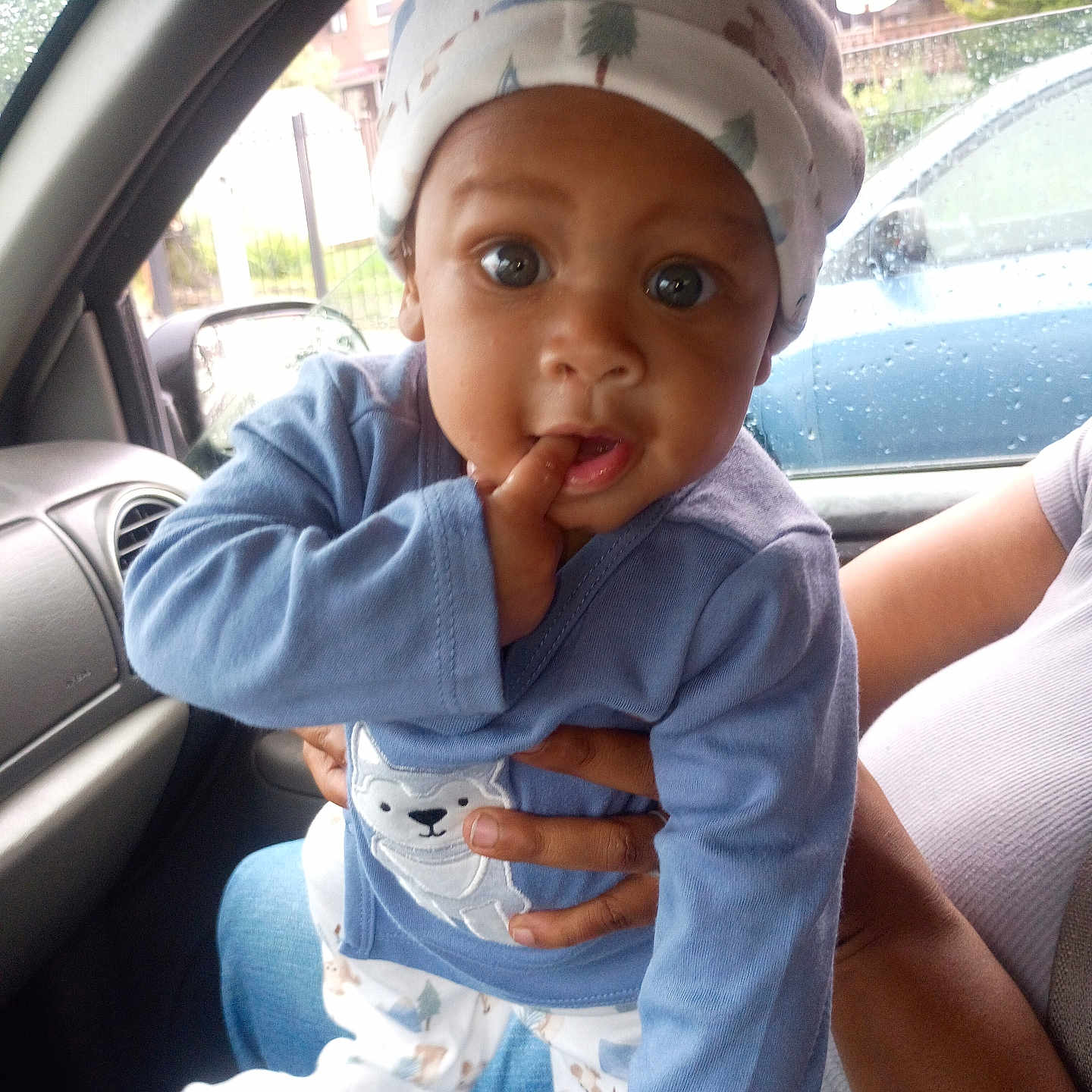 Aha'Mirrion Carroway is registered to the contest to win money with this photo: baby, child, infant, pajamas, hat, car_interior, raindrops, window, person, hand, blue_clothing, cute, curious, indoors, seated, portrait, face, expression, holding, casual