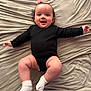 Jenaiah a rejoint le concours — aidez-le/la à gagner de superbes lots ! baby, infant, child, smiling, onesie, black_clothing, socks, bed, sheet, laying, happy, face, cheeks, curly_hair, hair_bow, portrait, indoor, cute, chubby_legs, baby_footwear