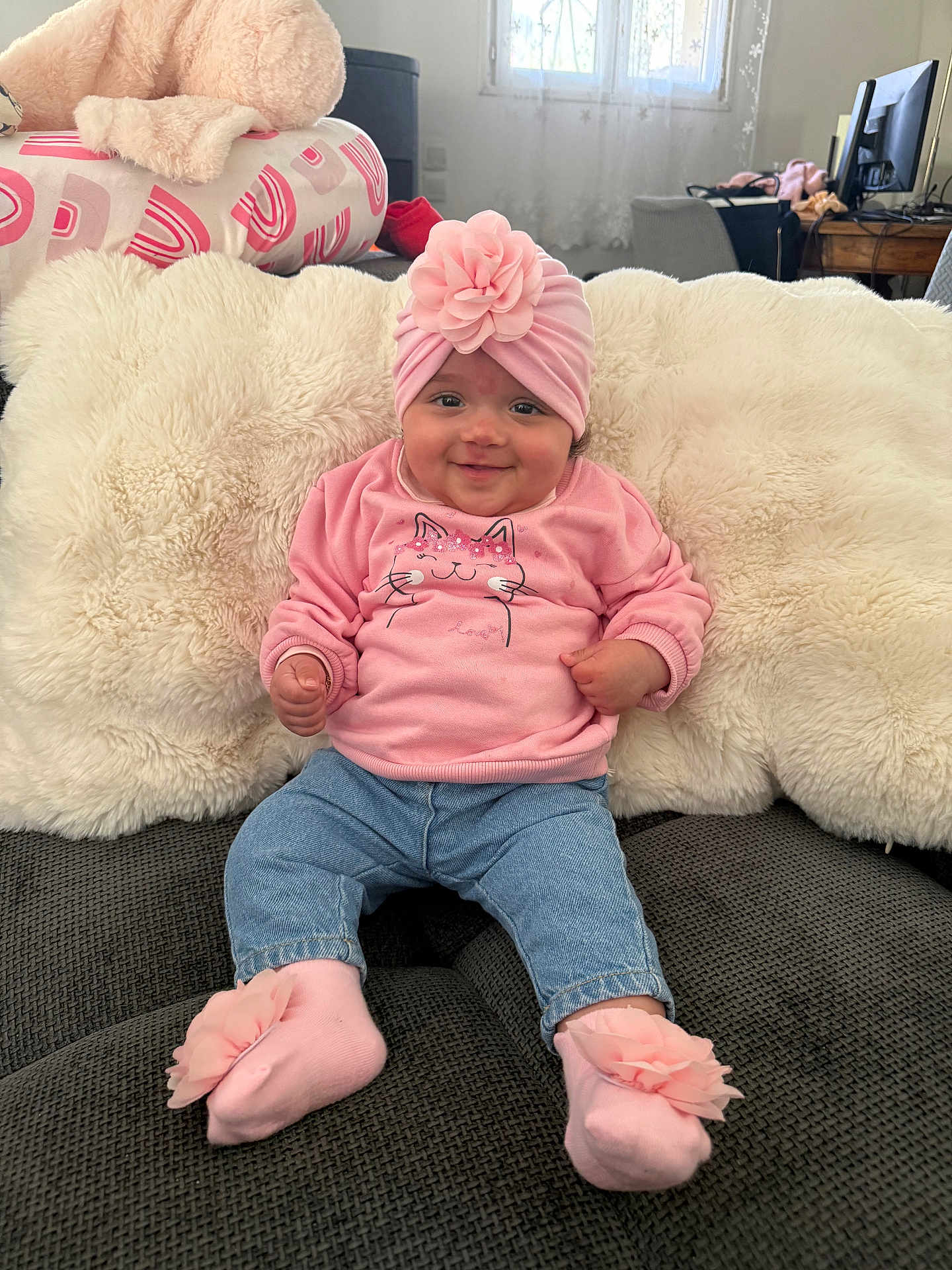 Jenaiah participe au concours pour gagner de l'argent avec cette photo : baby, infant, girl, smiling, pink_headband, flower_headband, pink_sweater, jeans, pink_socks, plush_pillow, white_fur, sofa, cushion, living_room, window, computer_monitor, cute, portrait, sitting, cozy
