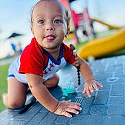 Daniel is registered to the contest to win money with this photo: baby, child, crawling, tongue_out, outdoor, playground, red_shirt, blue_sky, texture, curious, happy, person, infant, cute, daylight, toy, plastic_surface, hand, face, smiling