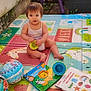 Léa a rejoint le concours — aidez-le/la à gagner de superbes lots ! toddler, child, toy, play_mat, book, outdoor, colorful, plastic_toy, person, sitting, baby, playtime, floor_mat, reading, cute, young_child, summer, daylight, happy, learning