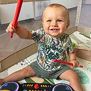 Manoé participe au concours pour gagner de l'argent avec cette photo : toddler, child, toy, drumsticks, drum_set, playpen, smile, happy, indoor, shorts, tshirt, colorful, floor_mat, baby, hands, legs, face, music, playing, cute