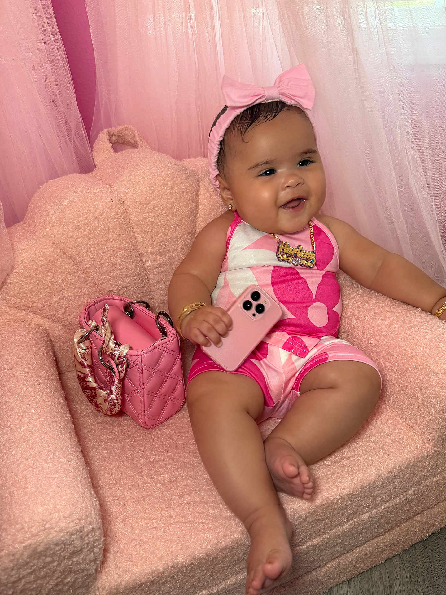 Harlem is registered to the contest to win money with this photo: baby, pink, chair, handbag, phone, headband, jewelry, smile, happy, infant, portrait, couch, fashion, accessory, furniture, child, indoors, cute, plush, person