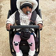 Fatoumata a rejoint le concours — aidez-le/la à gagner de superbes lots ! black_stroller, boots, child, cute, eyes, face, fur_trim, gloves, gravel, hands, hat, hood, outdoor, pacifier, pink_tights, seat_belt, stroller, toddler, winter, winter_clothing