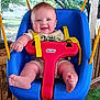 baby, child, swing, playground, outdoor, smiling, happy, blue_swing, yellow_straps, red_t_bar, grass, trees, wooden_fence, sunlight, cute, infant, person, seat, summer, daylight