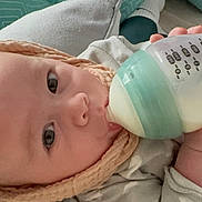Arthur is registered to the contest to win money with this photo: baby, bottle, milk, infant, face, hand, knit_hat, blanket, clothing, lying_down, cute, indoors, feeding, child, person, sleepwear, soft, comfort, closeup, peaceful