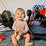 baby, infant, blue_eyes, wooden_toy, toy_car, motorcycle_helmet, motorcycle_gloves, red_toy_car, checkered_flag, wooden_blocks, blanket, smiling, sitting, indoors, child, cute, playtime, milestone, happy, portrait