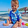 Caleb a rejoint le concours — aidez-le/la à gagner de superbes lots ! toddler, child, beach, ocean, sand, towel, blue_shirt, summer, sunny, water, people, mountain, vacation, outdoor, play, toy, casual_clothing, happy, portrait, sitting