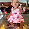 baby, bow, bracelet, child, face, furniture, glass, happy, headband, indoors, infant, lobster_pattern, photography, pink_dress, portrait, restaurant, sitting, smiling, table, wood_paneling