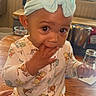 Jai-Lyanna joined the competition — help win amazing prizes! baby, bow, child, eyes, face, food, glassware, hand, headband, indoor, infant, pajamas, patterned_clothing, portrait, restaurant, sitting, smiling, table, winnie_the_pooh, wooden_table