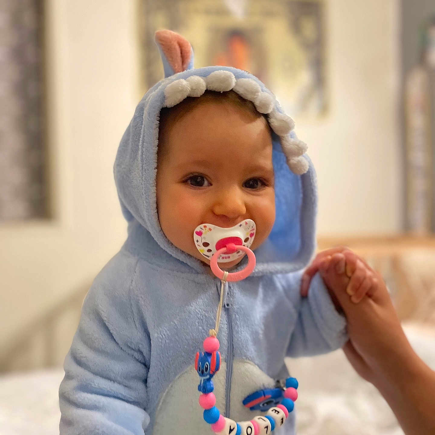 Eloa participe au concours pour gagner de l'argent avec cette photo : baby, bedroom, blue_onesie, child, clothing, cute, dinosaur_costume, face, hand_holding, hooded_outfit, indoor, infant, pacifier, person, portrait, smiling, soft_toys, toy_beads, warm_clothing, young_child