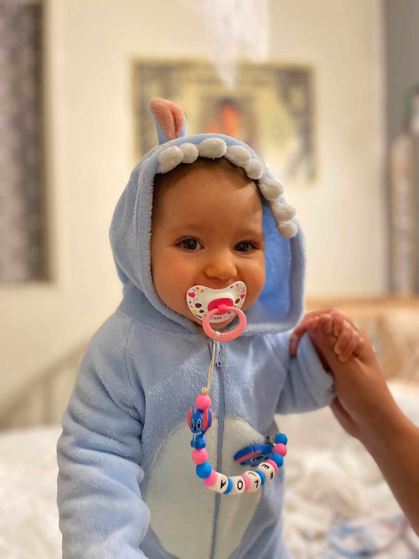 Eloa participe au concours pour gagner de l'argent avec cette photo : baby, child, pacifier, blue_onesie, dinosaur_costume, indoor, hand_holding, cute, smiling, face, portrait, soft_toys, bedroom, toy_beads, infant, person, clothing, hooded_outfit, young_child, warm_clothing