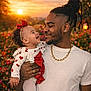 baby, child, dressed_up, family, father, flowers, gold_chain, happy, holding, love, man, nature, outdoor, portrait, red_bow, smiling, sunset, tattoo, toddler, white_clothing