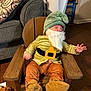 Jacob is registered to the contest to win money with this photo: baby, child, costume, gnome, beard, hat, wooden_chair, sleeping, indoors, floor, couch, pillow, laundry_basket, toy, plush_toy, clothing, footwear, hand, face, person