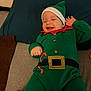 Jacob is registered to the contest to win money with this photo: baby, child, smiling, holiday_outfit, elf_costume, green_clothing, hat, couch, blanket, indoor, happy, infant, cute, button, belt, red_collar, hand, face, relaxed, cozy