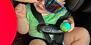 Jacob is registered to the contest to win money with this photo: baby, child, car_seat, sunglasses, toy, hand, seatbelt, infant, colorful, playful, closeup, person, casual, cute, indoor, wearing, holding, legs, clothing, seat